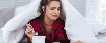 heartbroken woman eats snacks in bed after bad breakup